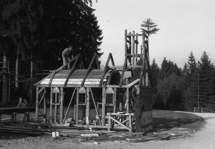 Beim Aufbau im Salzburger Freilichtmuseum, 1983. Das Holzgerüst steht. Auch beim Glockienturm bis zum Spitz. Das Gewölbe ist eingeschalt und sichtbar. Der Firstbaum hängt am Glockenturm.