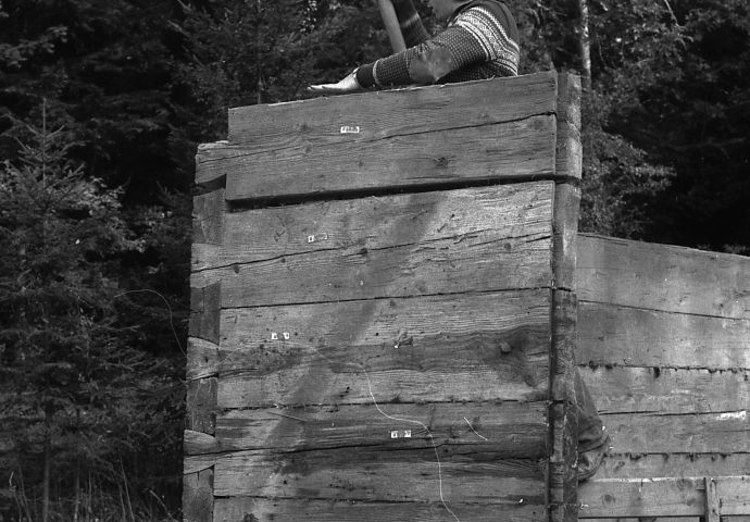 Beim Aufbau im Freilichtmuseum, 1983. Ein Zimmerer bearbeitet fügt mit einem Holzhammer Eckelemente vom Baukörper zusammen.