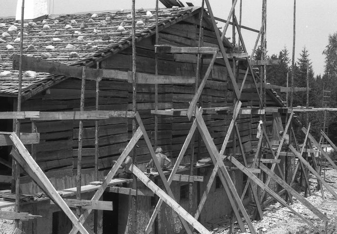 Beim Aufbau im Freilichtmuseum, 1983. Blick auf die Rückseite. Das Haus ist eingerüstet. Das Dach ist bereits mit einem Legeschindeldach belegt. Die Wand ist mit querliegenden Holzbrettern verkleidet.