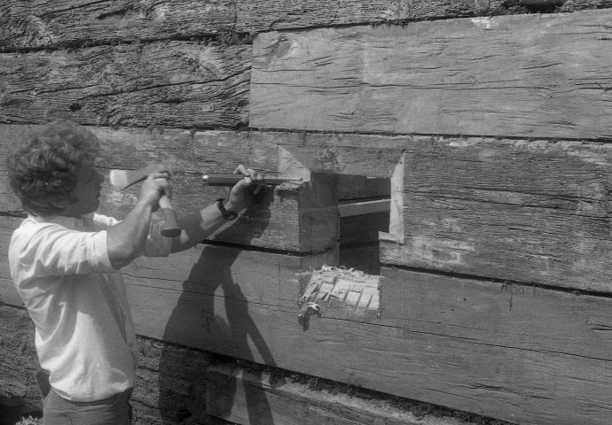 Beim Aufbau im Freilichtmuseum, 1982. Ein Zimmerer bearbeitet die Fensteröffnung mit Hammer und Beitel.