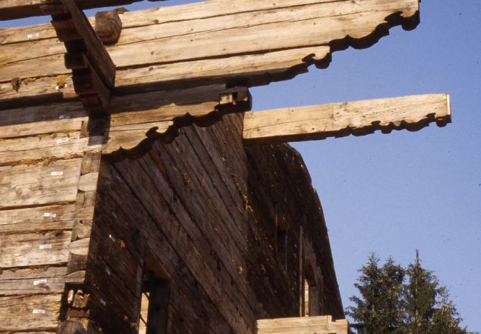 Beim Aufbau im Salzburger Freilichtmuseum, 1980. Blick von unten gegen die vorstehenden Giebelbalken. Diese sind mit Dekorelementen behauen.