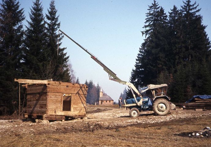 Beim Aufbau im Salzburger Freilichtmuseum, 1984. Der Grundstock ist bereits gestellt. Ein Arbeitstraktor hebt Balken auf die bereits bestehende Konstruktion.