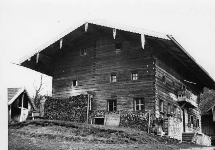 Das Haus an seinem ursprünglichen Standort in Nußdorf, 1938. Das Haus steht leicht erhöht, der Fotograf steht leicht rechts, so dass übers Eck zwei Seiten sichtbar sind. Auf der rechten Seite führen Steinstufen zur Tür. Holzbeigen rund ums Haus.