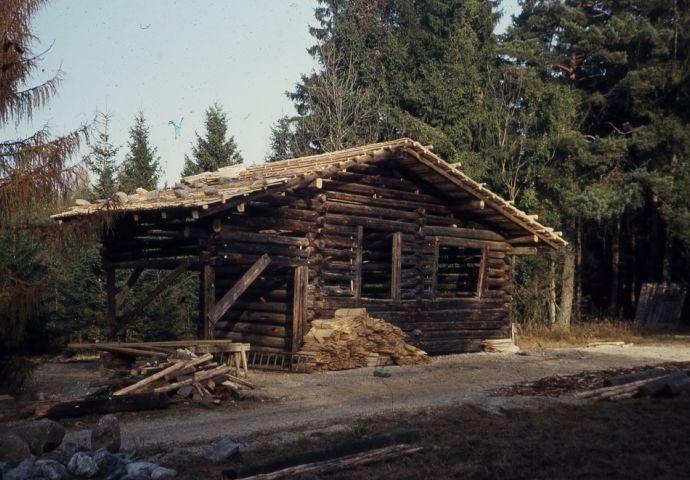 Beim Aufbau im Freilichtmuseum, 1984. Das Haust steht bereits vollständig da. Die Fenster fehlen. An der linken Seite des Hauses ist Holz aufgeschichtet. Die Baustelle sieht sehr ordentlich aus.